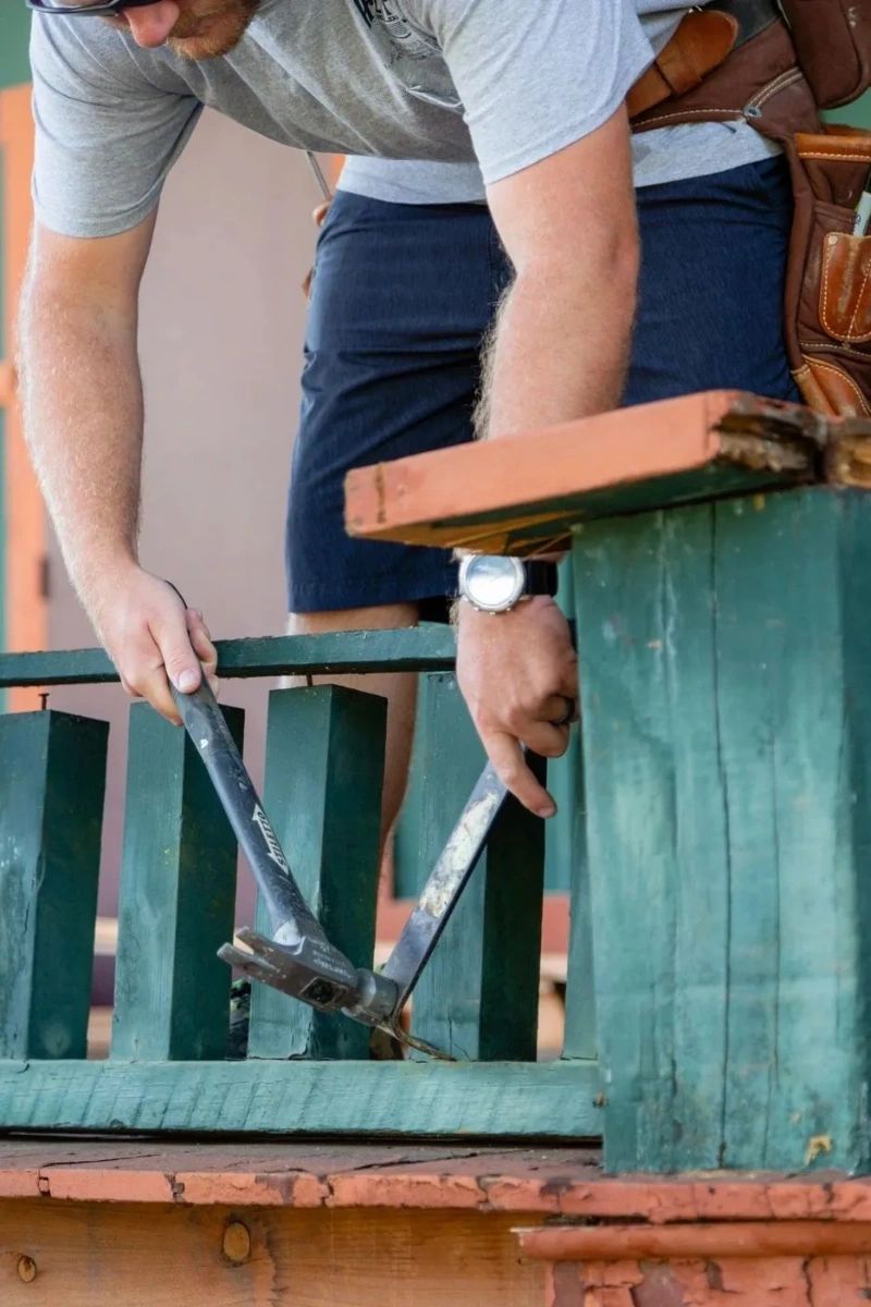 Man repairing a small fence on the front porch of a house.