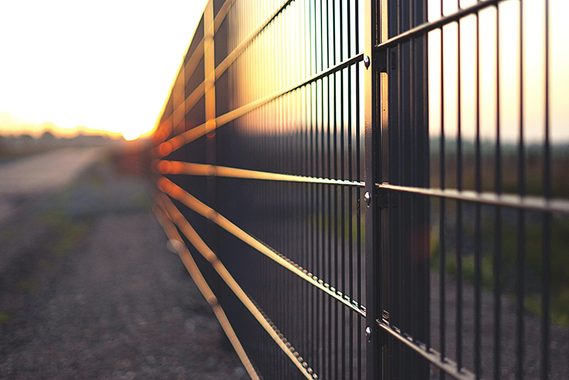 Metal commercial fence between a field and highway.