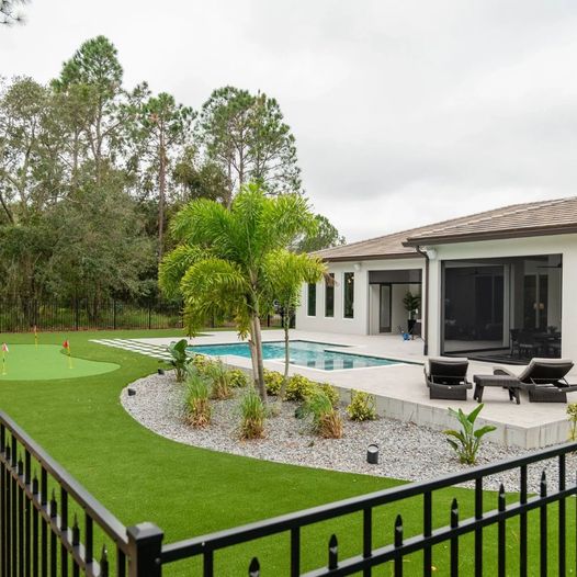 House with metal fence and a tree in the center of the yard.